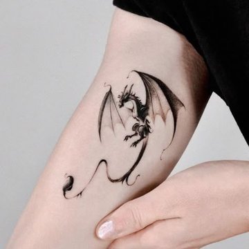 Delikatny smok w stylu fine line na ramieniu