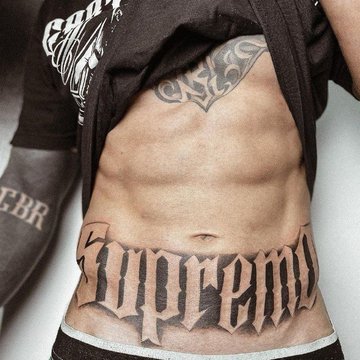 Tatuaż z napisem Supreme na męskim brzuchu