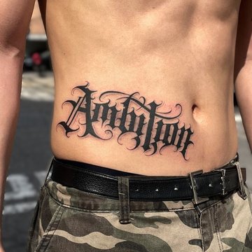 Tatuaż z napisem Ambition na męskim brzuchu