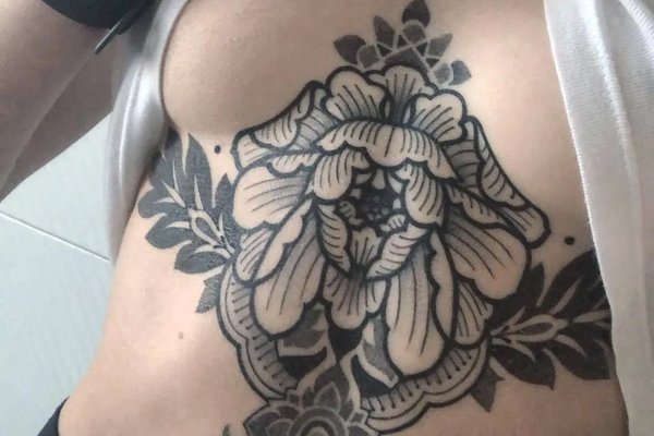 czarny tatuaż na całym brzuchu kobiety z mandalą i elementami blackwork